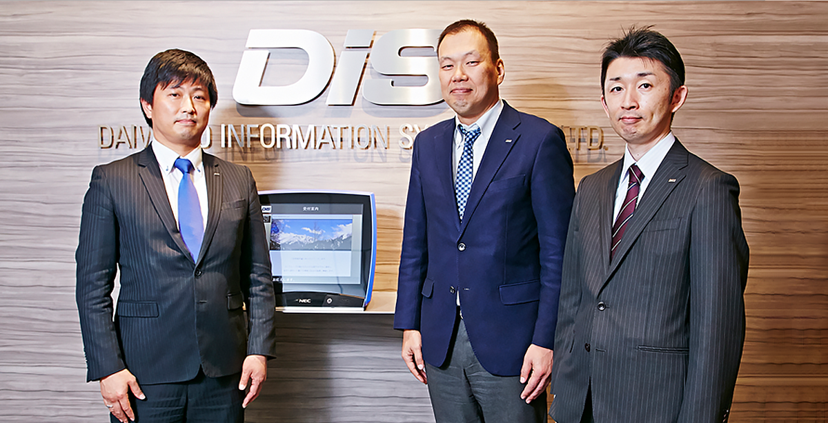 ダイワボウ情報システム株式会社のエントランスに並ぶ3人の男性 左:販売推進本部 販売推進第2部 PH1グループ 次世代プラットフォーム推進グループ 副部長 谷水茂樹氏、中央:システム推進部 部長付 藤田光徳氏、右:システム推進部 イントラネット課 係長 岩谷圭祐氏